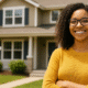 Young woman smiling outside a rental home with a "For Rent" sign in the front yard.