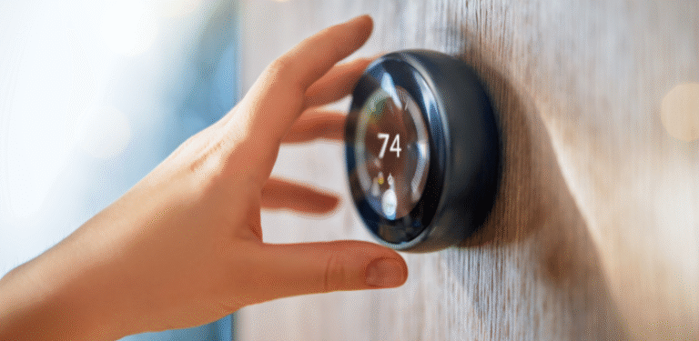 Hand adjusting a smart thermostat set to 74 degrees, illustrating the convenience and energy efficiency of modern home technology for rental properties.