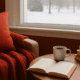Cozy winter reading nook with a red blanket, open book, and warm coffee by a snowy window.