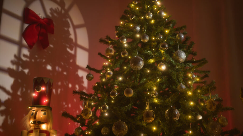 A cozy, safely decorated artificial Christmas tree lit with warm white lights and ornaments, positioned indoors next to a lighted nutcracker figure.
