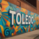 Colorful Toledo mural painted on the side of a historic brick building along a quiet sidewalk in downtown Toledo.