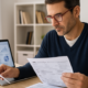 Property owner reviewing tax documents, receipts, and financial statements at a desk with a laptop displaying rental income reports.